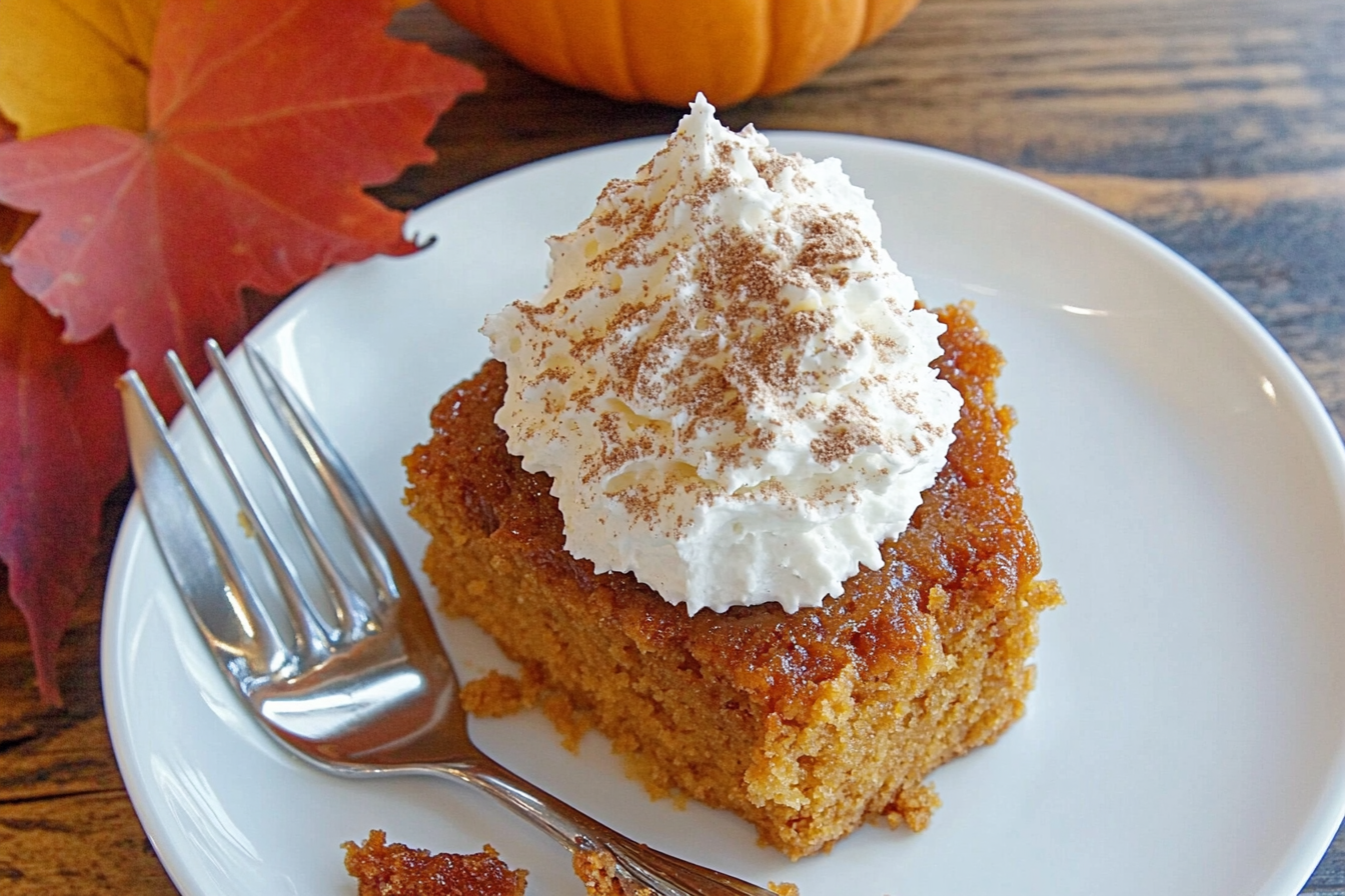 "Freshly baked pumpkin dump cake in a glass baking dish, topped with golden crispy layers, surrounded by autumn leaves and cinnamon sticks."